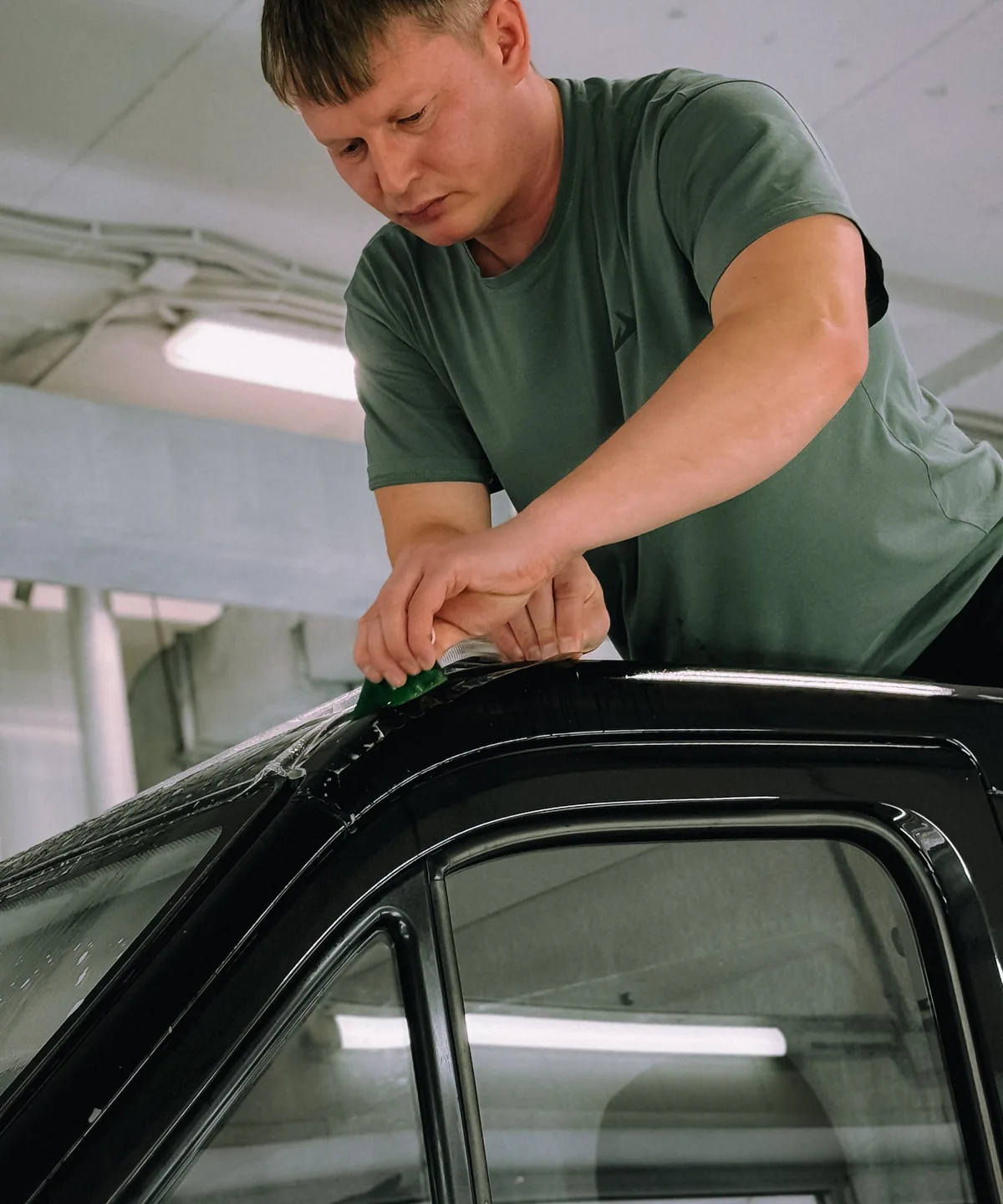 Instalador aplicando película no vidro de um carro preto, com a espátula sobre a borda da janela